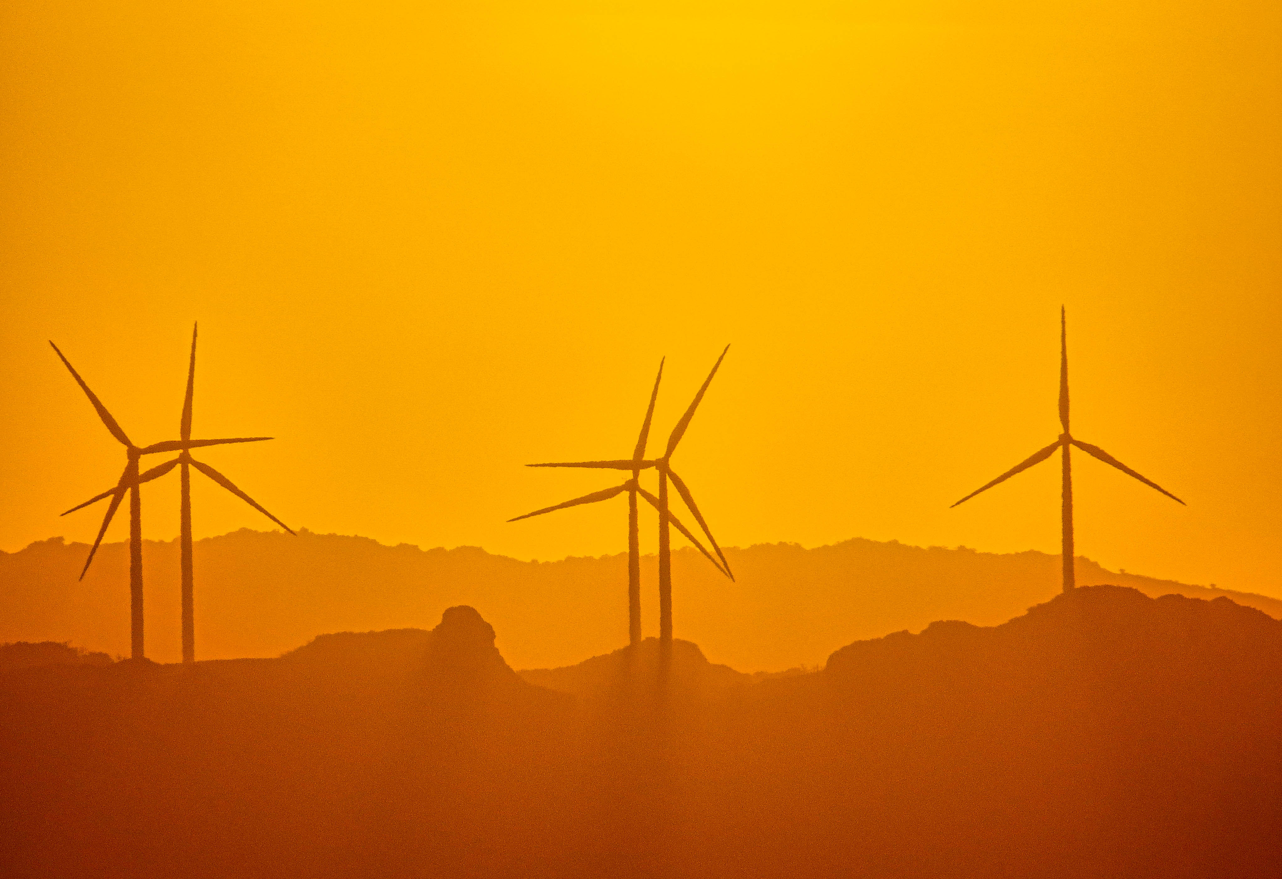 Wind turbines imaged from many kilometers away the equivalent of a 1000mm focal length as the sun begins to set over the hills and mountains in north coastal Luzon Island, The Philippines.